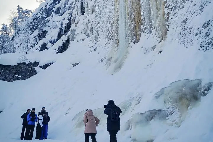 A small guided group standing beneath the frozen cliffs of Korouoma Canyon